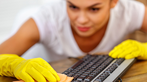 Woman with dark hair wearing yellow rubber cleaning gloves using a rag to clean a computer keyboard