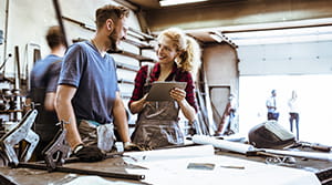 Brown hair bearded man speaking with blonde woman in a welding shop