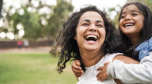 Mother carrying daughter on her back and smiling