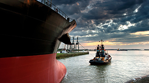 A tug boat pulling a cargo ship out to sea from a canal or harbor at sunrise or sunset