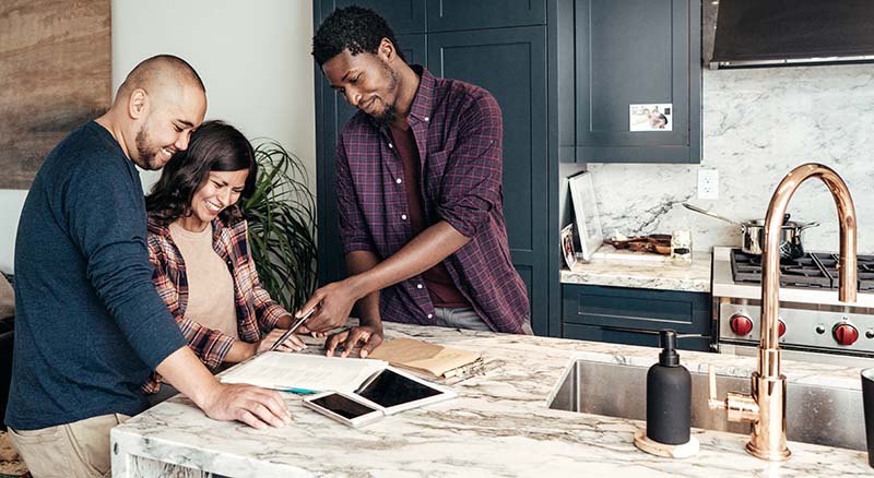 Three people looking at paperwork in kitchen