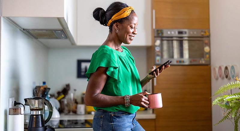 Person in kitchen looking at phone with mug in hand