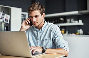 Man on phone looking at accounts on laptop