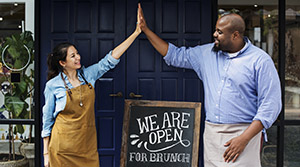 Shop owners giving high fives in front of we are open sign