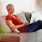 Woman types on laptop while relaxing on couch