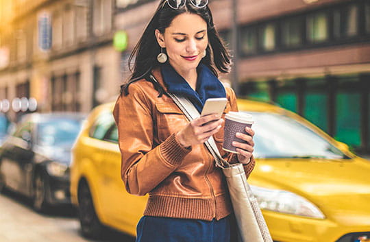 A woman checks her phone as she walks through the city