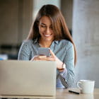 Smiling woman checks smartphone while working at laptop