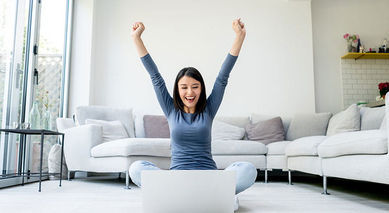 A woman throws her hands in the air excitedly in front of her computer