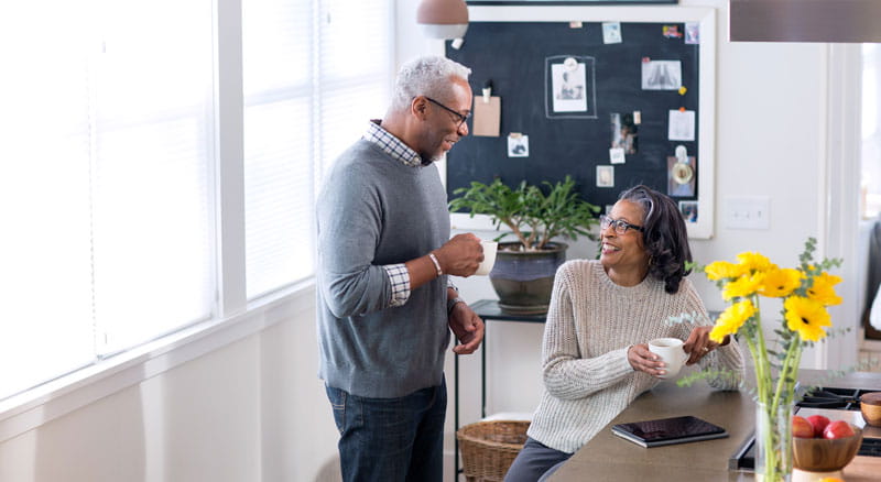 Older man and woman drink coffee in the kitchen while accessing Banner Online Banking using a tablet device
