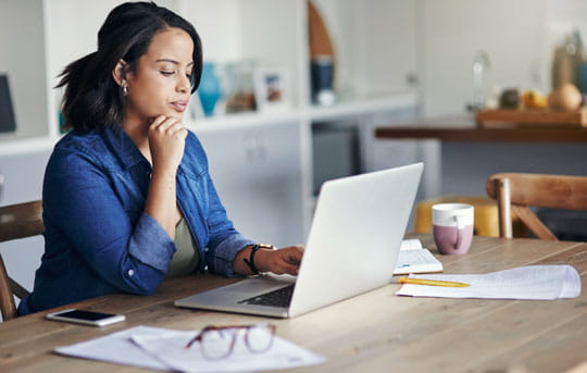 Woman sits at dining room table using laptop