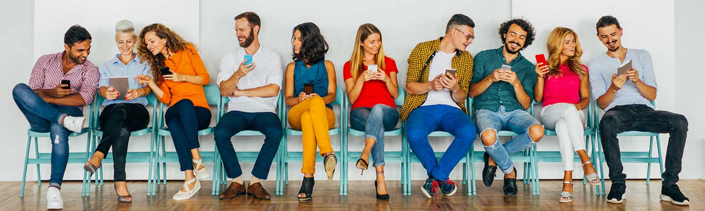 A row of people in colorful clothes sitting on folding chairs checking mobile phones