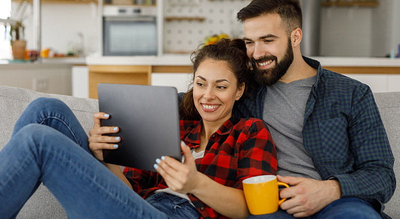 A couple curled up on the couch reviewing their PFM budget on a digital device