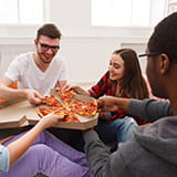 Four college students pulling a slice of pizza from a pizza box