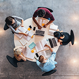 Photo taken directly above, looking down at a round table with 5 college students studying