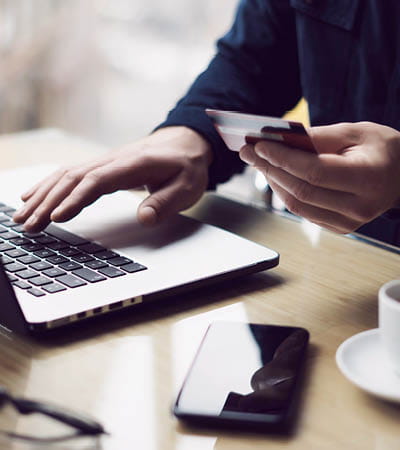 Person typing with one hand and a credit card in the other hand