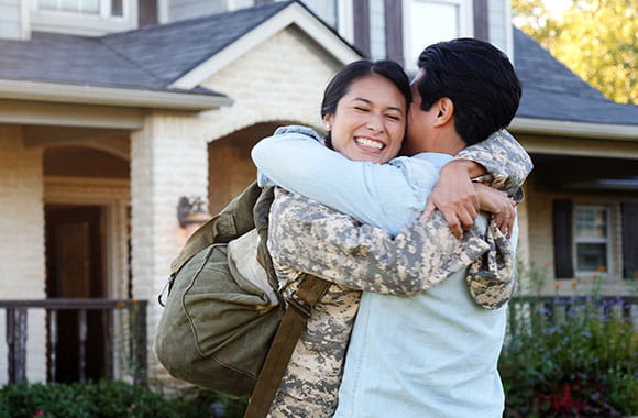 Person in uniform hugging another in front of home
