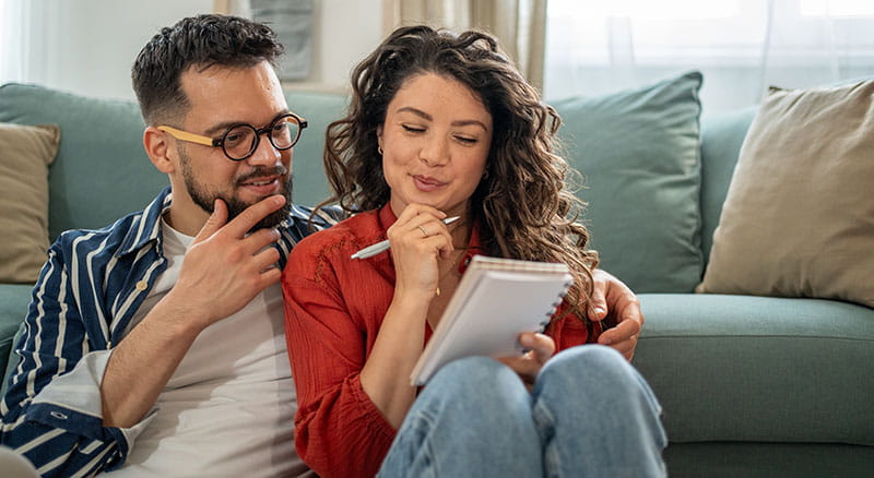 Two people looking at notepad sitting near couch