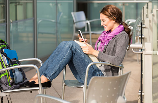 Woman sits outdoors looking at smartphone