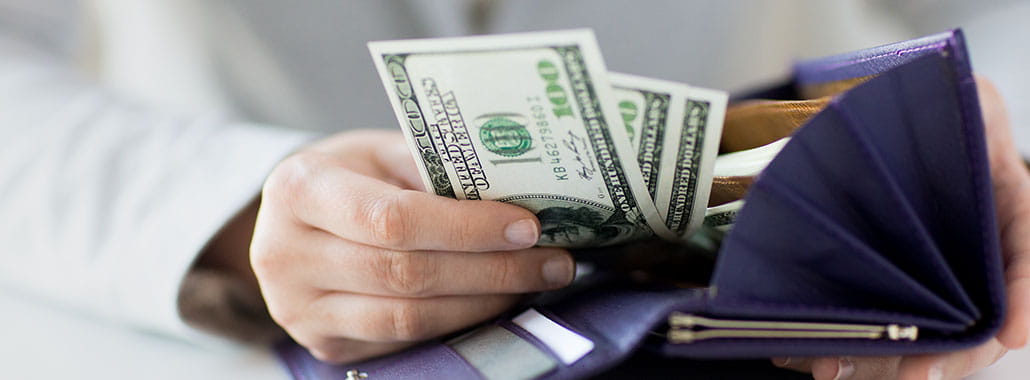 Person putting $100 bills in wallet