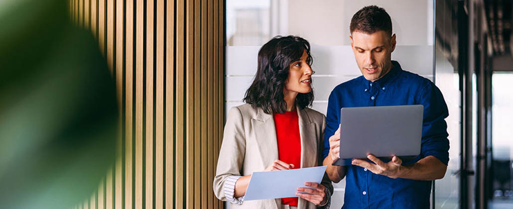 Two people walking in office with laptop and paper