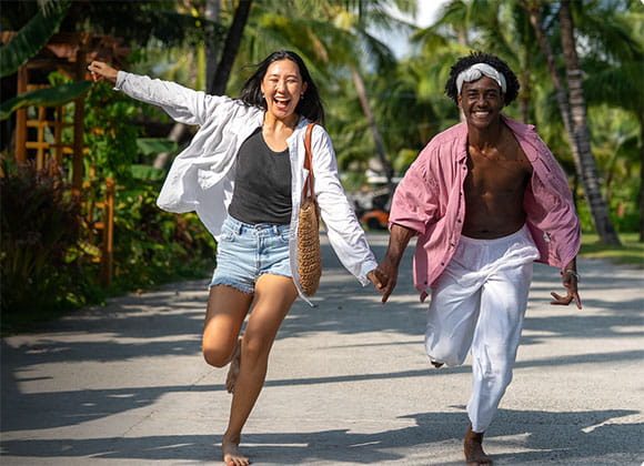 Two people running and laughing in a tropical location with priceless logo
