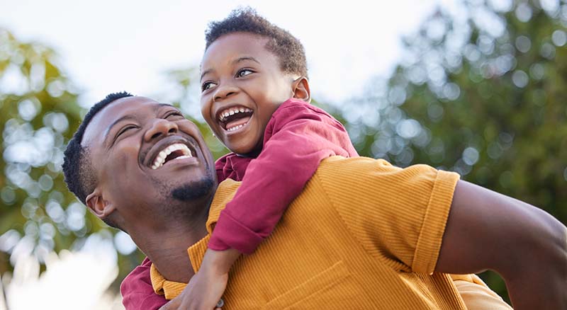 Man giving a child a piggyback ride and smiling