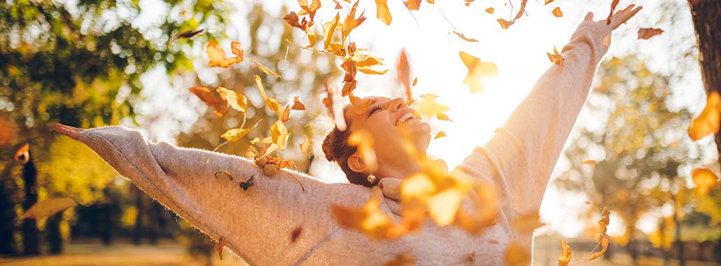 Person smiling and throwing fall leaves in the air