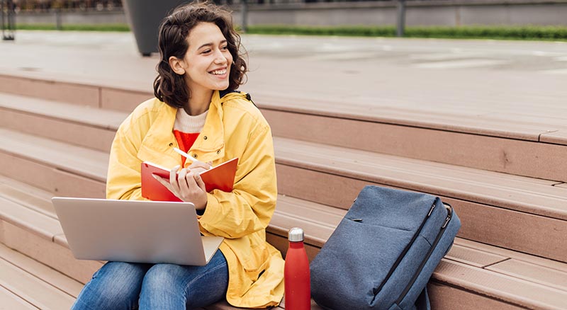 Person smiling on steps with notebook and laptop