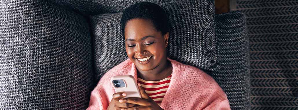 Person smiling while looking at phone on couch