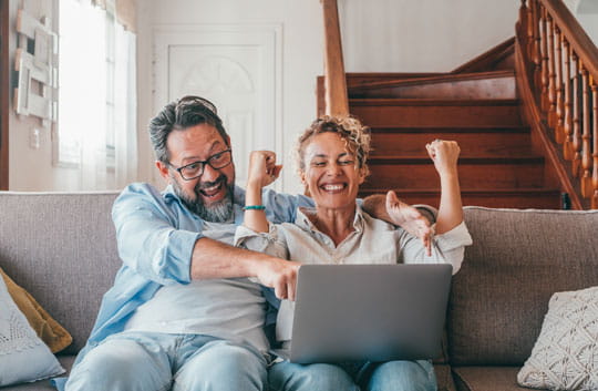 Excited couple on sofa looking at laptop