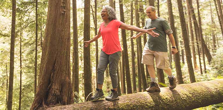 Two people walking across a log in a forest