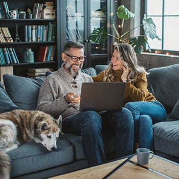 Two people looking at laptop on couch with dog