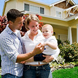 Young couple holding baby stands in front of their first home, financed with a mortgage from Banner Bank