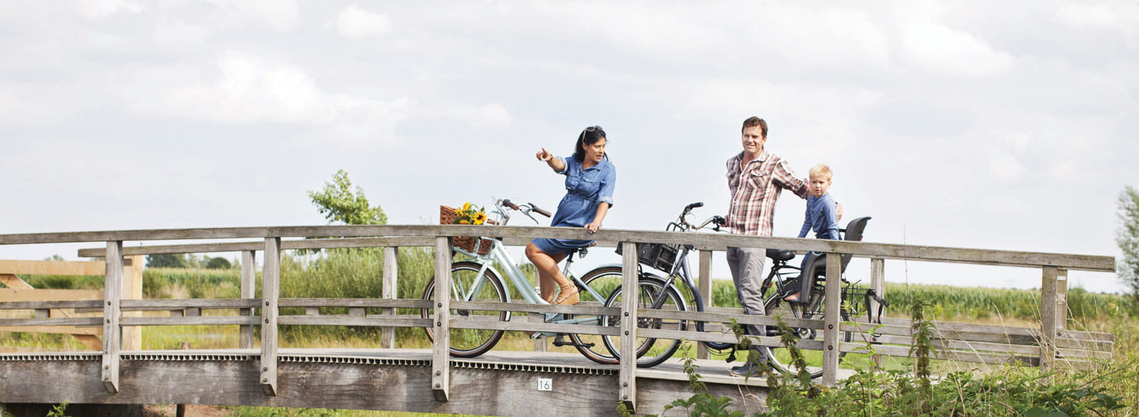 Family of three rides their bikes over a wooden bridge