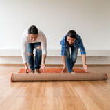 Man and woman unroll area rug onto wood floor