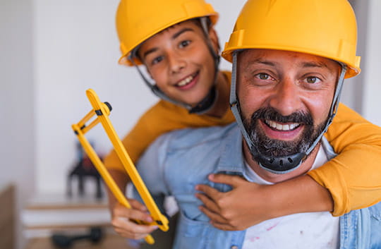 A father and young son in yellow hard hats smiling while working on improvements