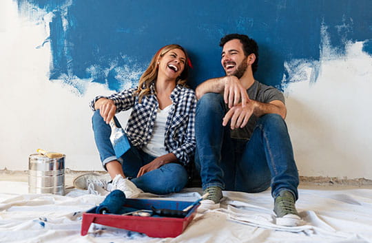 A couple laughs together while painting their wall