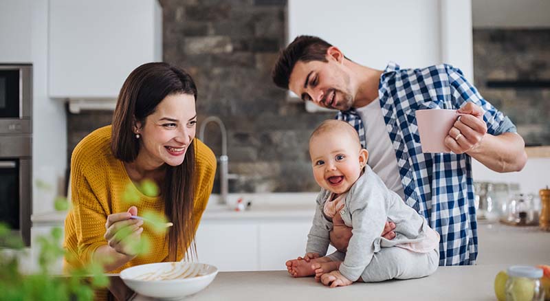 Couple together in kitchen feeding their baby who is sitting on the counter