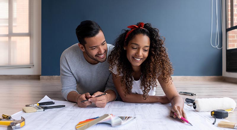 Young couple laying on their living room floor looking at remodel plans