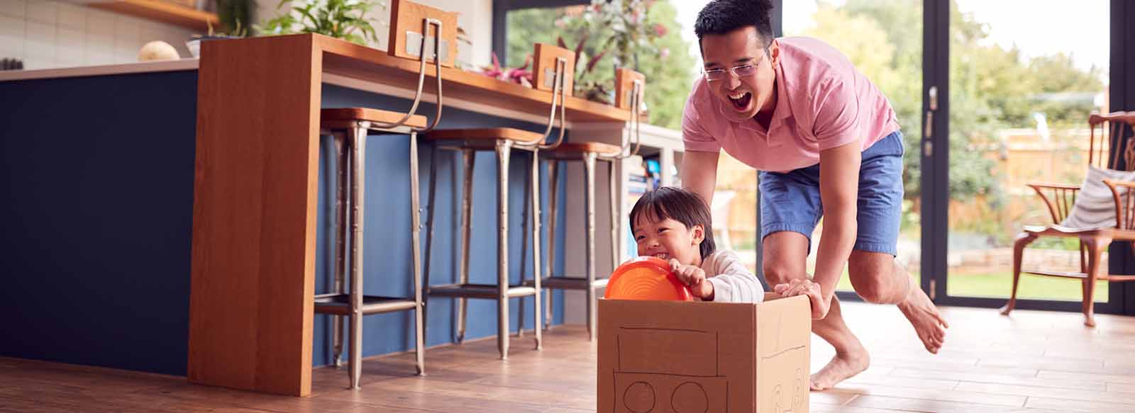Father pushing son in cardboard box at home