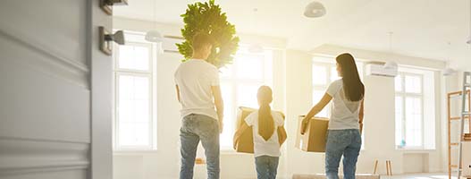 Three people moving boxes into an empty home