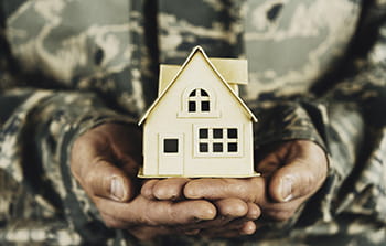 Military member holding cardboard house in their hands