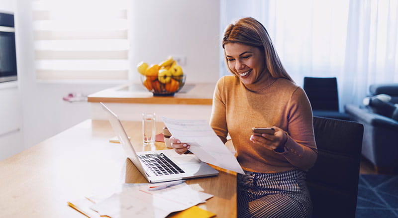 Woman looking at paperwork with laptop and phone