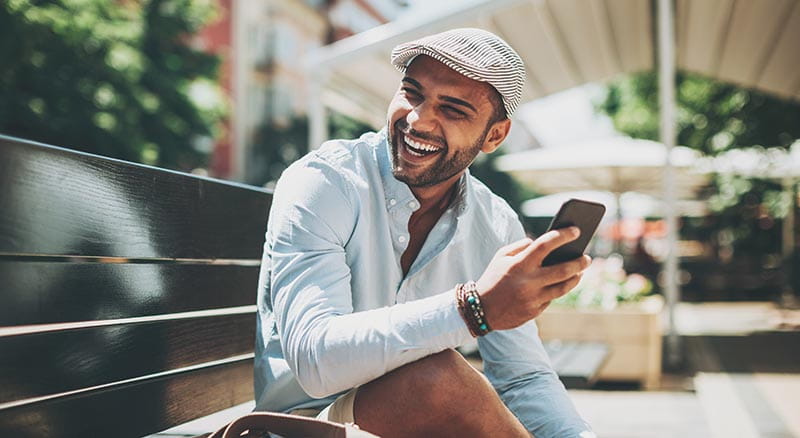 Person sitting on bench smiling with phone in hand
