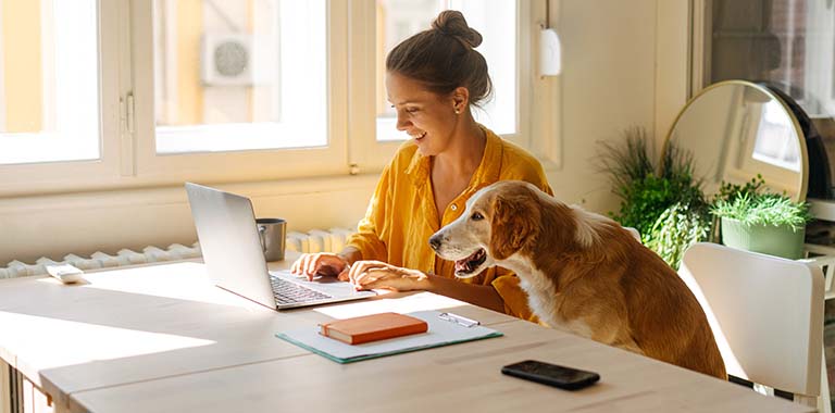 Person at a desk smiling at a laptop next to a dog
