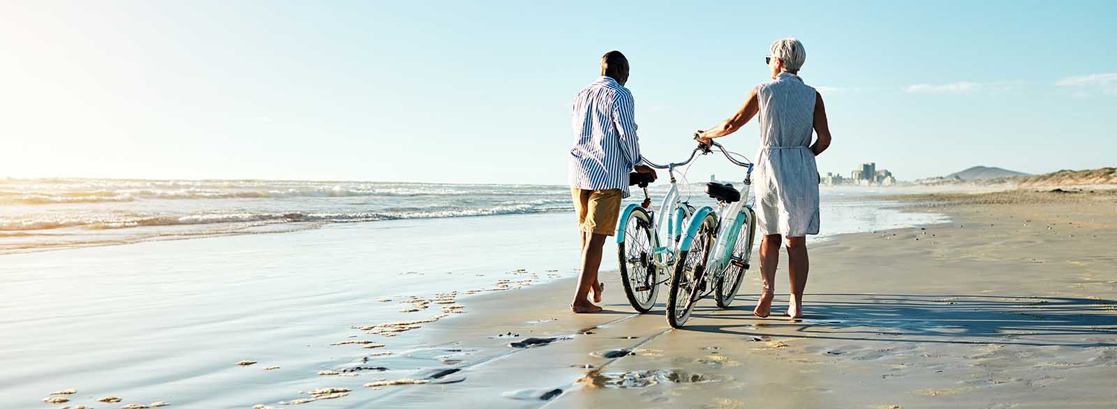 Two people walking a bike on the beach