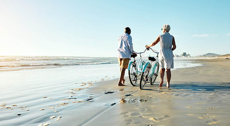Two people walking a bike on the beach