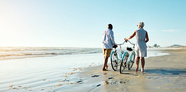Two people walking a bike on the beach