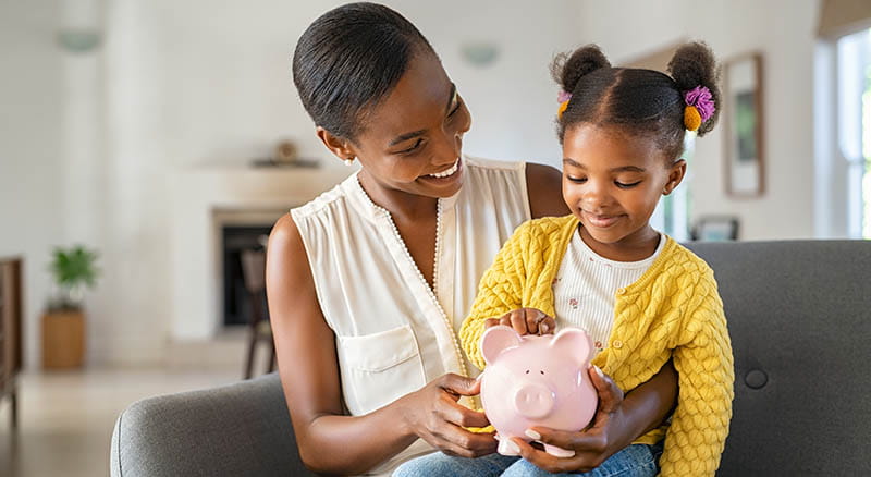 Mother showing child how to put money in a piggy bank