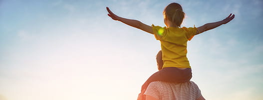 Child on parents shoulders with arms wide open